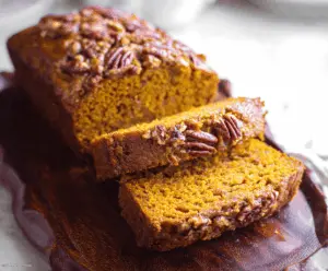 Freshly baked pumpkin pecan bread with a golden crust, topped with chopped pecans and a dusting of powdered sugar, perfect for fall baking.