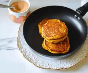 Fluffy pumpkin ricotta pancakes topped with maple syrup and garnished with cinnamon and fresh whipped cream on a rustic plate