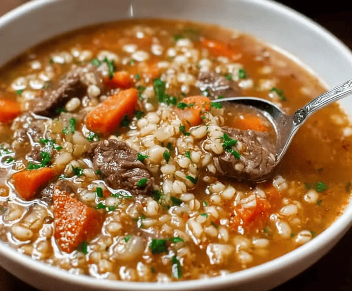 Hearty beef and barley soup with tender beef chunks, fresh vegetables, and steaming broth in a rustic bowl