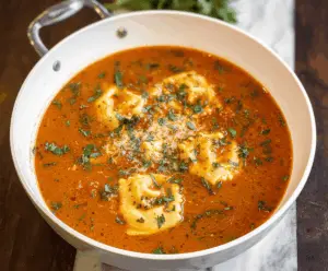 A steaming bowl of ravioli soup garnished with fresh herbs, showcasing tender ravioli pasta in a flavorful broth with vegetables.
